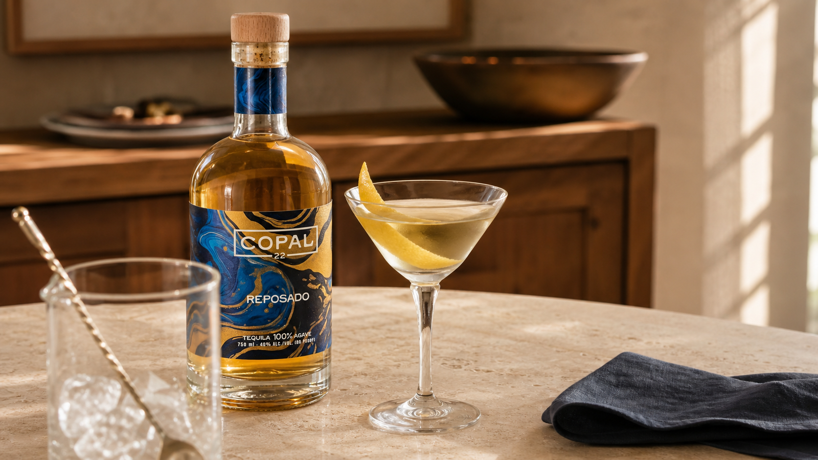 Copal 22 Reposado beside a dry tequila martini with a lemon peel on a parchment stone sideboard