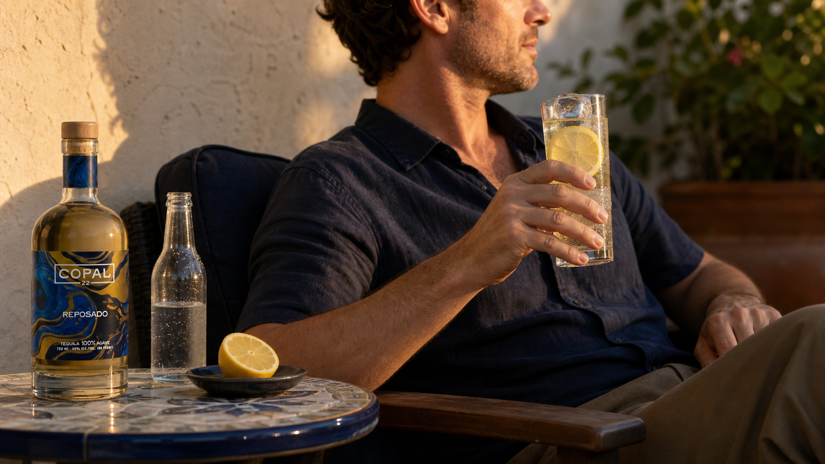 An adult enjoying a pale reposado tequila Collins beside a Copal 22 bottle on a sunset patio