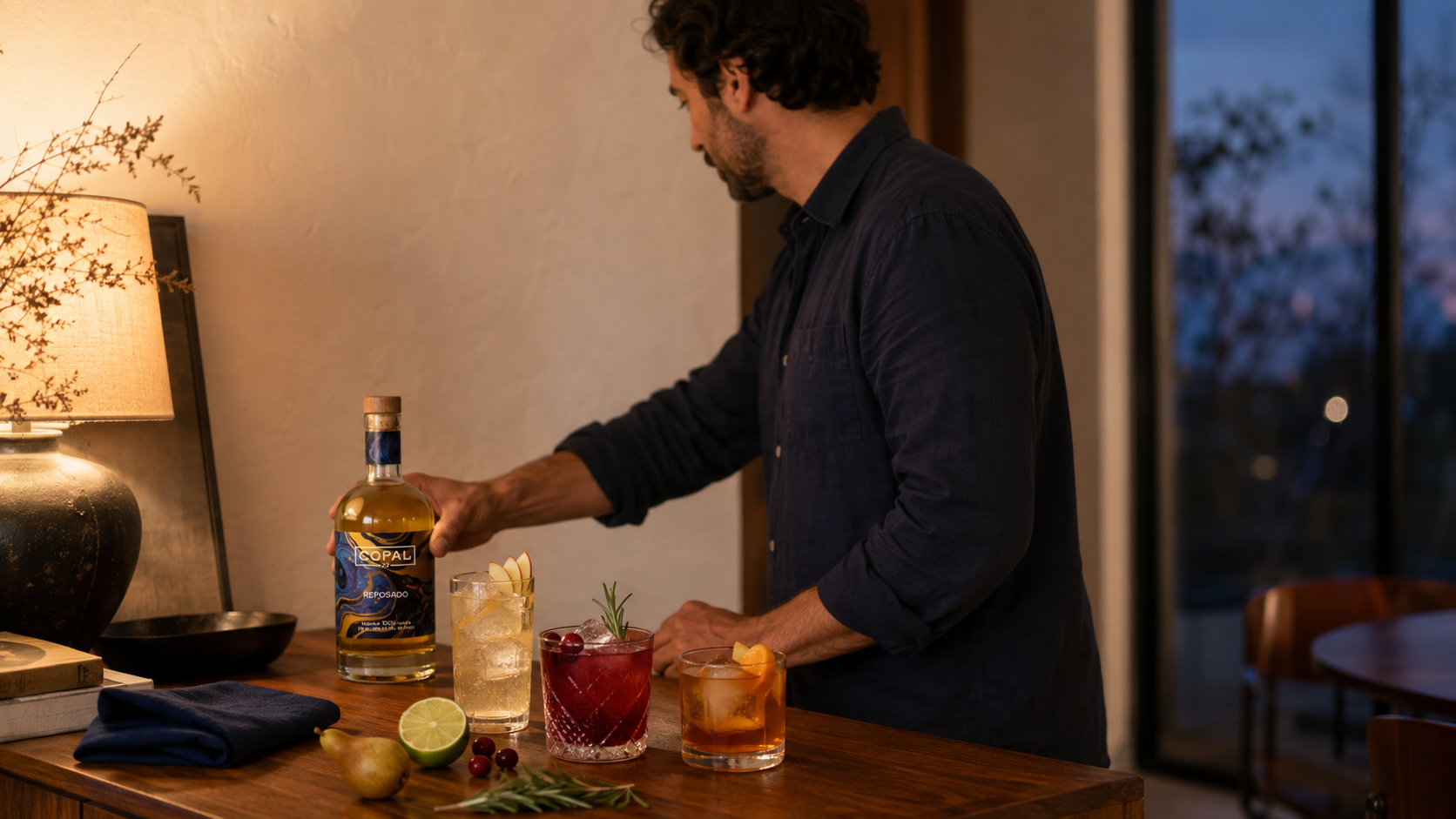 Adult setting a Copal 22 reposado bottle beside three restrained fall tequila cocktails on a walnut sideboard